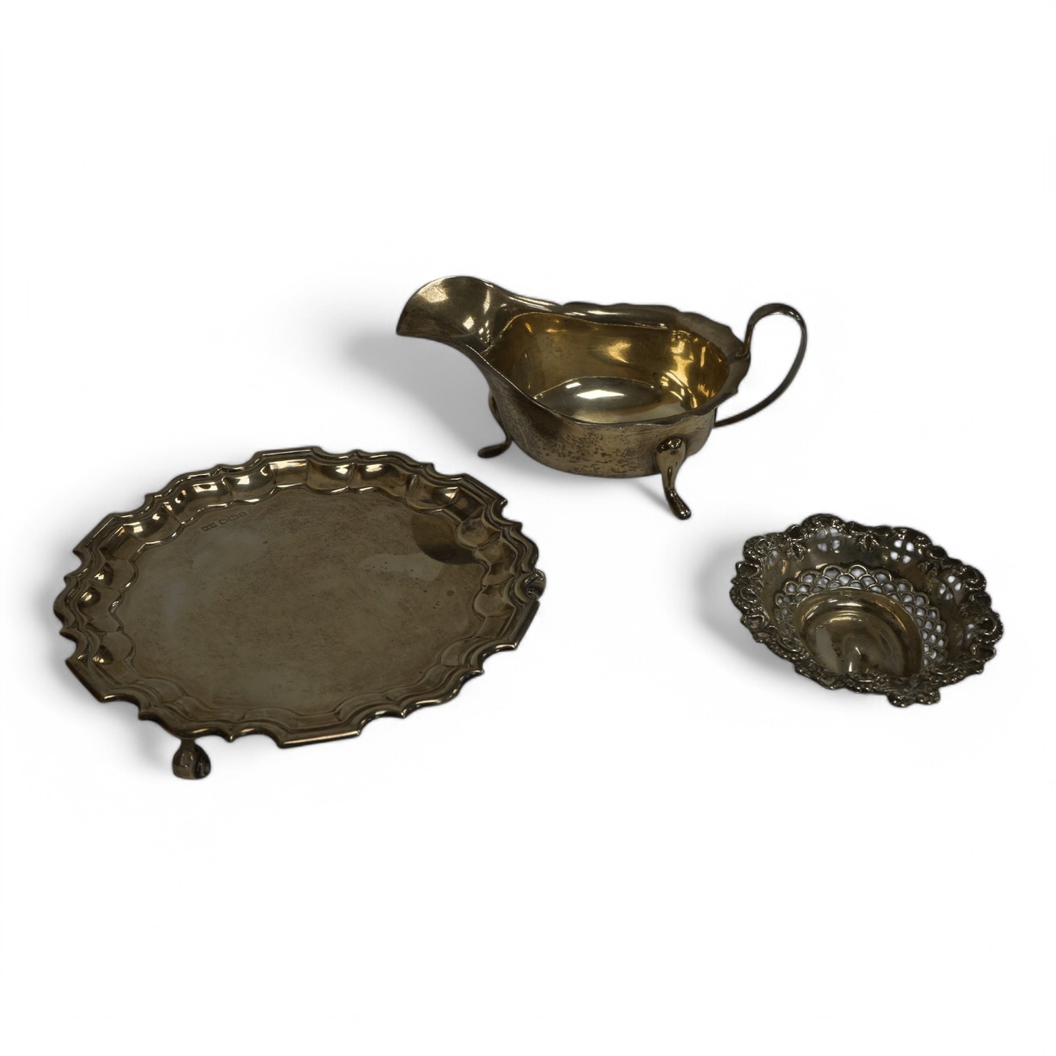 A George V silver waiter, by Walker & Hall, with pie crust border on three scroll feet, Sheffield, 1923, 15.6cm, together with a George V silver sauceboat and a small repousse silver bonbon dish, 9.9oz. Condition - fair